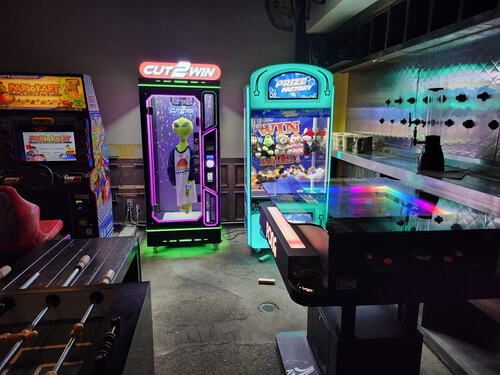 Photo of various games at Crickets Draft House & Grill in Waco, Texas. Clockwise, from top left corner: Mario Kart Arcade GP, Cut 2 Win, Prize Factory (claw machine game), Table Pong, and a foosball table. 