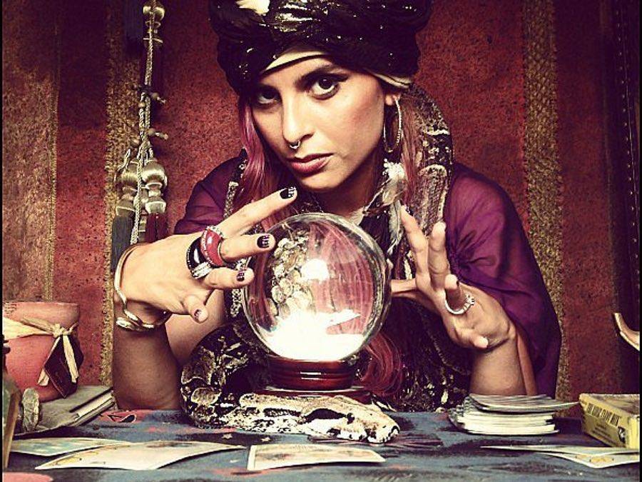 Photograph of a gypsy looking into the camera, her hands hovering above a crystal ball